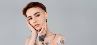 Gri pankartta izole edilmiş, yüzü dokunan genç bir kadın.