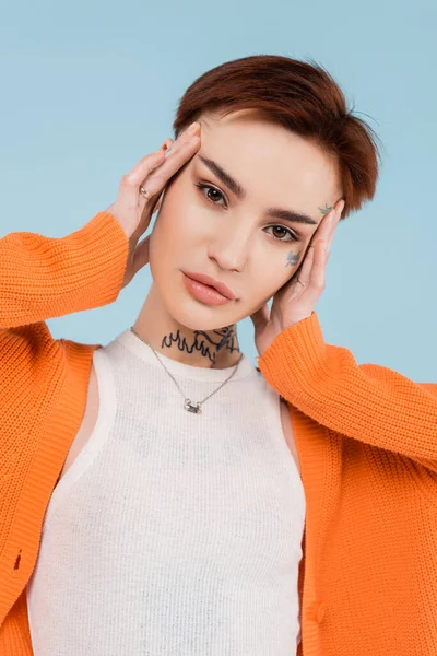 young woman with tattoos in orange cardigan posing isolated on blue
