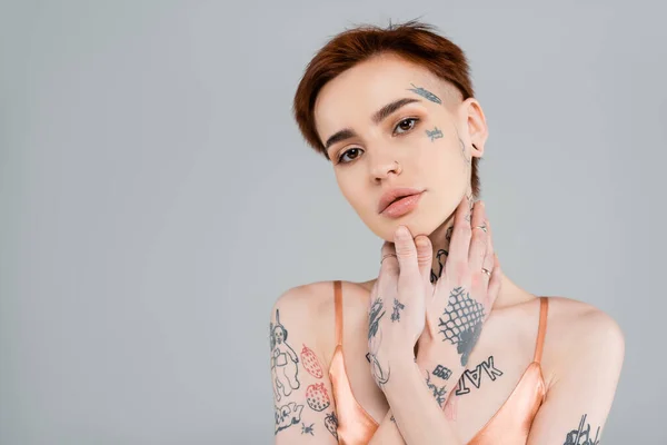 young tattooed woman looking at camera isolated on grey