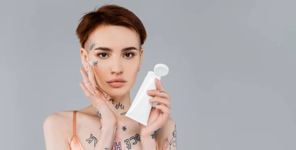 Mladá Žena Tetováním Drží Bílou Trubici Nanáší Krém Obličej Izolované — Stock fotografie