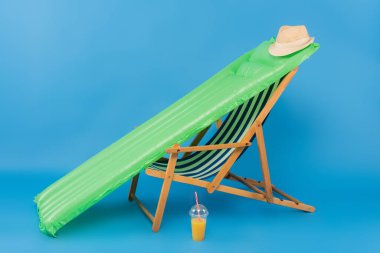 Sun hat on inflatable mattress near deck chair and orange juice on blue background  clipart