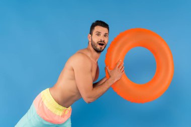 Şişme yüzüğü mavi renkte tutan şaşkın gömleksiz adam. 