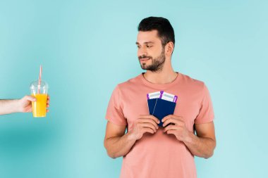 Elinde portakal suyu olan plastik bardaklı bir adam mavi arka planda pasaportlu bir gezgin. 