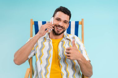 Gülümseyen adam güvertedeki sandalyede tek başına akıllı telefondan konuşuyor gibi. 