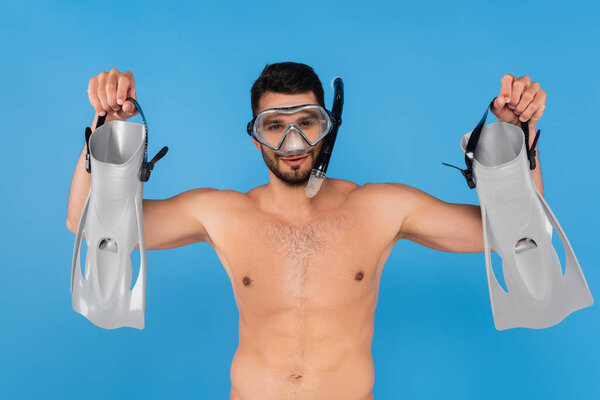 Shirtless man in swimming goggles holding flippers isolated on blue 