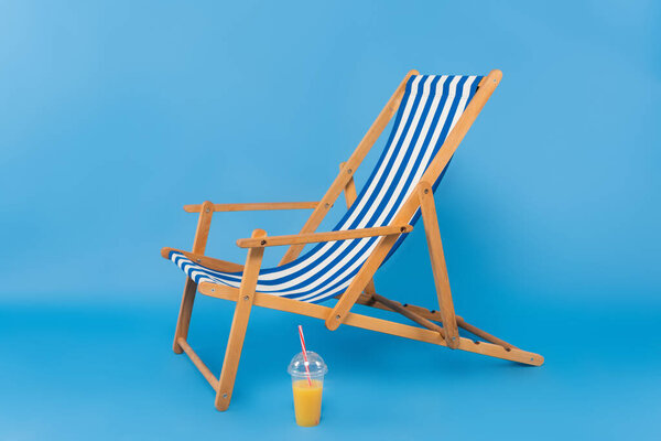 Orange juice near deck chair on blue background 