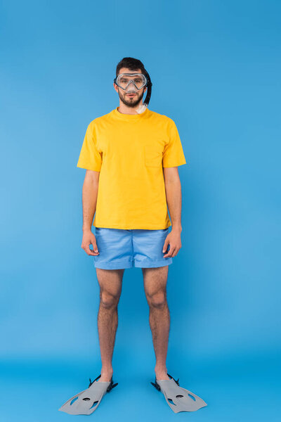 Man in shimming goggles and flippers looking at camera on blue background 