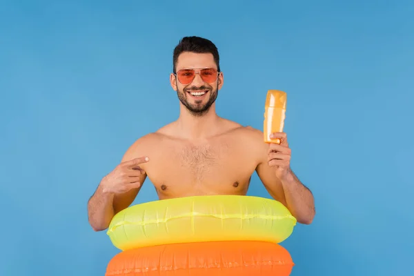 Smiling Man Sunglasses Inflatable Rings Pointing Sunscreen Isolated Blue — Stock Photo, Image