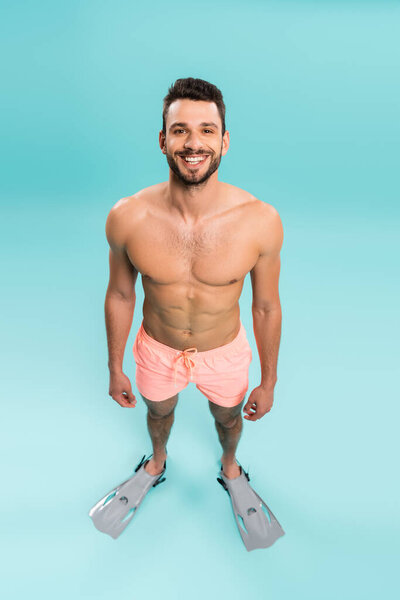 High angle view of smiling man in shorts and swimming flippers on blue background 