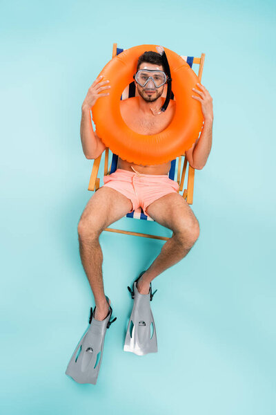 High angle view of man in swimming goggles holding inflatable ring on blue background 