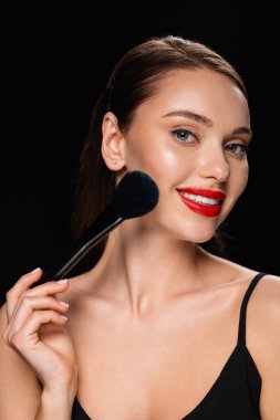 smiling woman powdering face with cosmetic brush isolated on black clipart