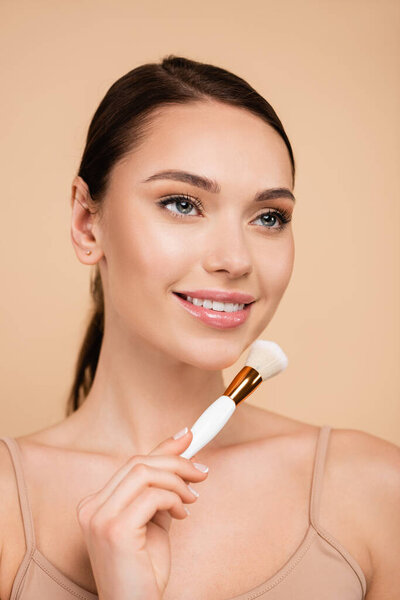 happy woman with natural makeup holding cosmetic brush isolated on beige