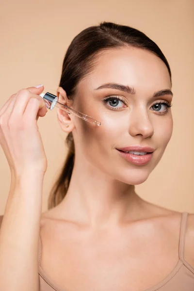 Young Woman Looking Camera While Applying Cosmetic Serum Isolated Beige — Stock Photo, Image