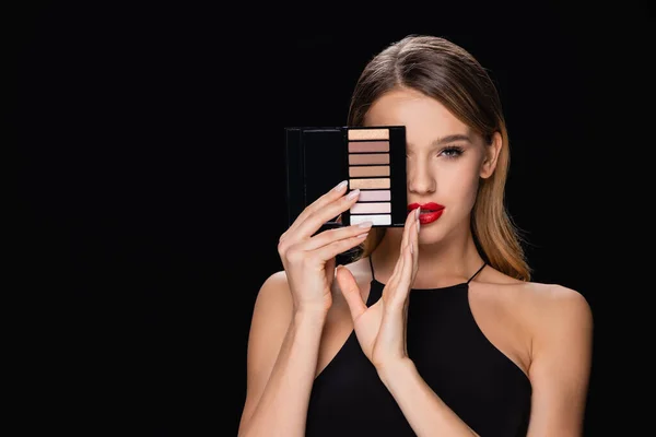 young woman obscuring face with eye shadows palette isolated on black