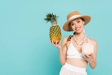 Güneş şapkalı güzel kadın elinde ananas ve hindistan cevizli kokteyl tutuyordu. 