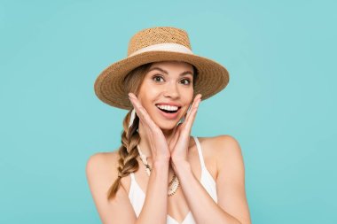 Cheerful woman in straw hat looking at camera isolated on blue  clipart