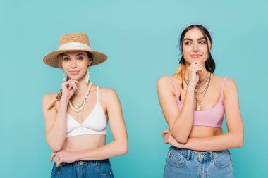 Güneş şapkalı ve bandanalı gülümseyen kadınlar mavi üzerinde yalnız poz veriyorlar. 