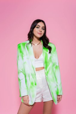 Ceketli şık bir kadın pembe arka planda kameraya bakıyor. 