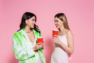 Pembe arka planda plastik bardaklar tutan genç arkadaşlar 