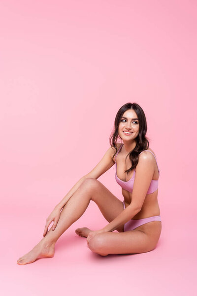 Веселая брюнетка в купальнике сидит на розовом фоне 