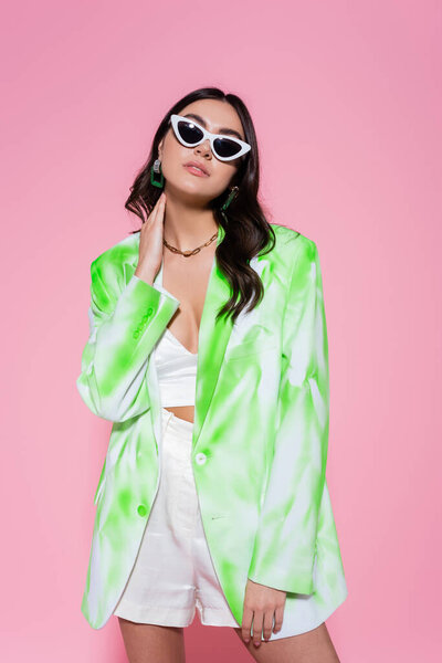 Stylish woman in sunglasses and jacket posing on pink background 