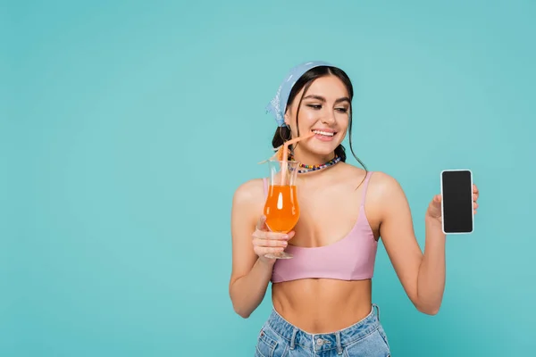 Pretty woman with cocktail holding smartphone with blank screen isolated on blue
