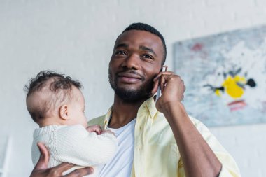Pozitif Afro-Amerikalı bir adam cep telefonuyla konuşurken kucağında çocuk tutuyor.