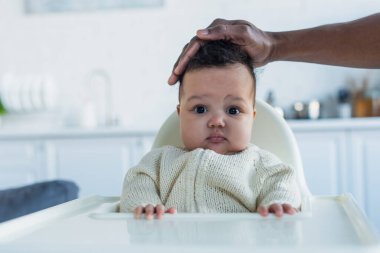 Afro-Amerikan babası bebek koltuğunda oturan bebek kızına dokunuyor.