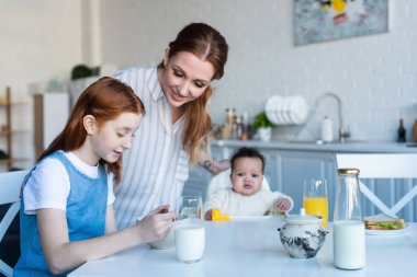 Mutfakta kahvaltıda ırklar arası kızların yanında gülümseyen bir kadın.