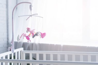 soft toys hanging over crib in nursery near window clipart