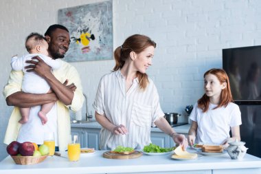 Çok ırklı bir ailenin yanında kahvaltı hazırlayan mutlu kadın.
