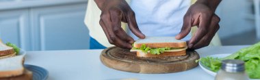 partial view of african american man making sandwich on chopping board, banner clipart