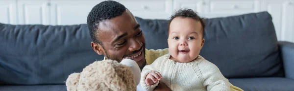 Alegre Bebé Mirando Cámara Cerca Africano Americano Padre Osito Peluche — Foto de Stock