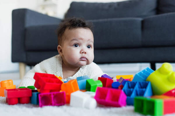 african american baby girl crawling on floor near blurred colorful building blocks