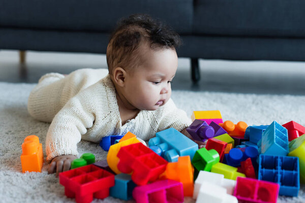 african american child in knitted romper on floor near multicolored building blocks