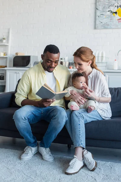 Smiling Woman Sitting Sofa Baby African American Husband Reading Book — Stock Photo, Image