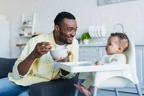 Hombre Afroamericano Feliz Sosteniendo Tazón Cerca Niño Sentado Una Silla —  Fotos de Stock