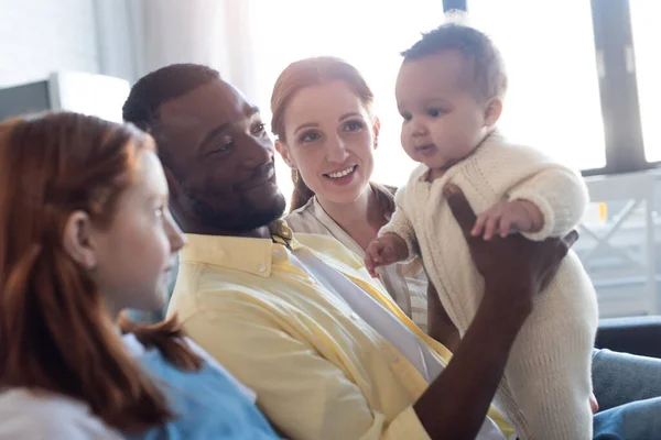 Gülümseyen Afrikalı Amerikalı Baba Bebeğini Bulanık Ailesinin Yanında Tutuyor — Stok fotoğraf