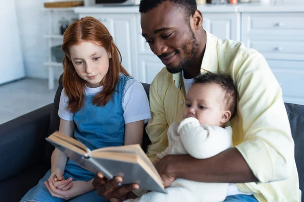 Sonriente Afroamericano Hombre Leyendo Libro Interracial Hijas Casa —  Fotos de Stock