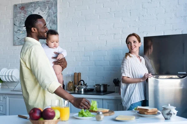 Africano Americano Hombre Holding Bebé Mientras Preparar Sándwiches Cerca Feliz — Foto de Stock