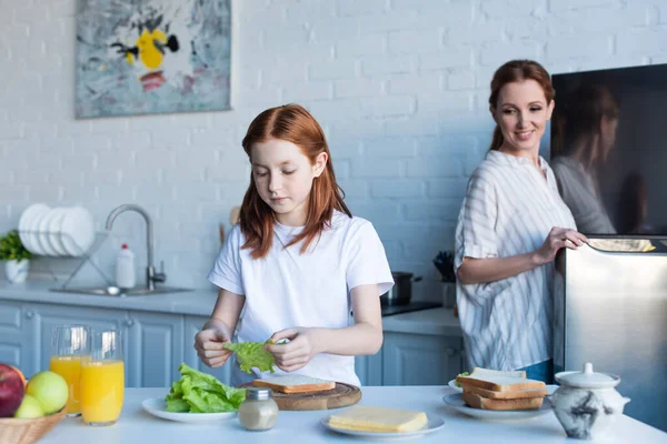 Pelirroja Chica Preparando Sándwiches Para Desayuno Cerca Feliz Mamá — Foto de Stock