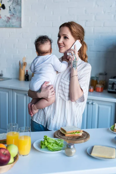 Smiling Woman Talking Smartphone While Holding African American Daughter Table — Stock Photo, Image