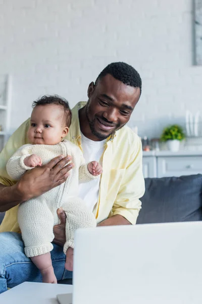 Alegre Afroamericano Hombre Sentado Cerca Borrosa Portátil Con Bebé Niño — Foto de Stock