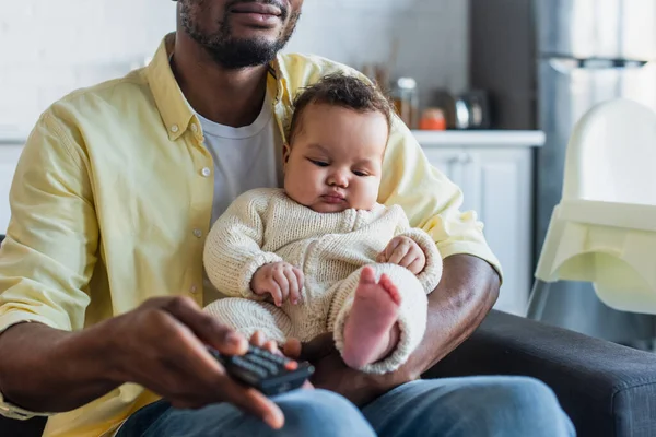 非洲裔美国人一边拿着遥控器一边和小女儿在家里看电视 — 图库照片