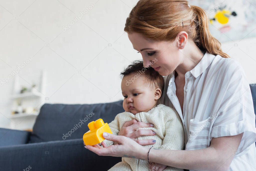mother holding building block near little african american daughter