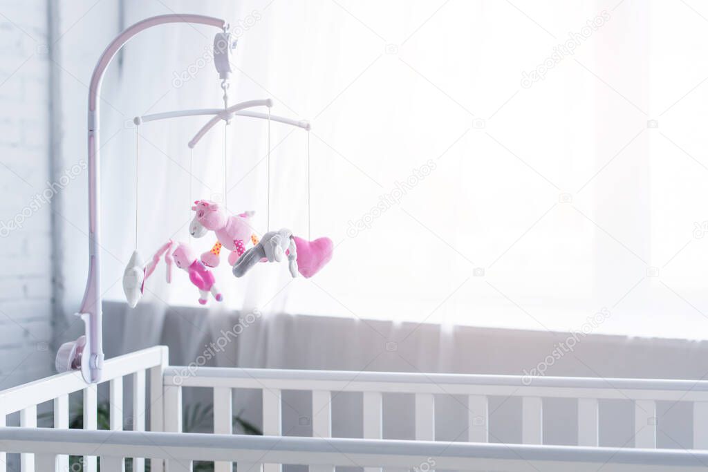 soft toys hanging over crib in nursery near window