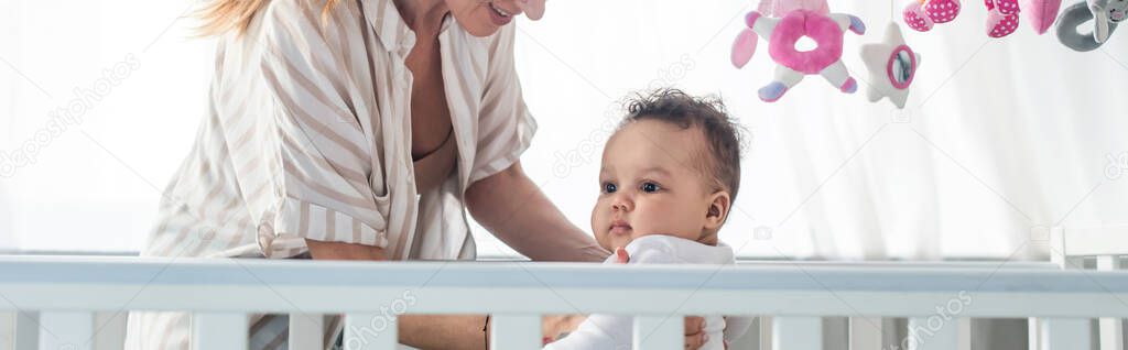 woman smiling near infant african american child in crib, banner