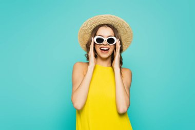 Positive woman in straw hat and sunglasses isolated on blue  clipart