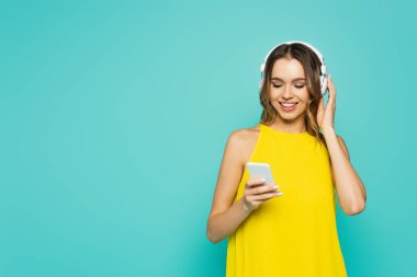 Mavi üzerine izole edilmiş kulaklık ve akıllı telefon kullanan gülümseyen kadın. 