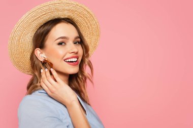 Pretty woman in sun hat listening music in earphone isolated on pink  clipart